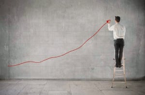 Man standing on ladder drawing upwards trending red arrow across wall