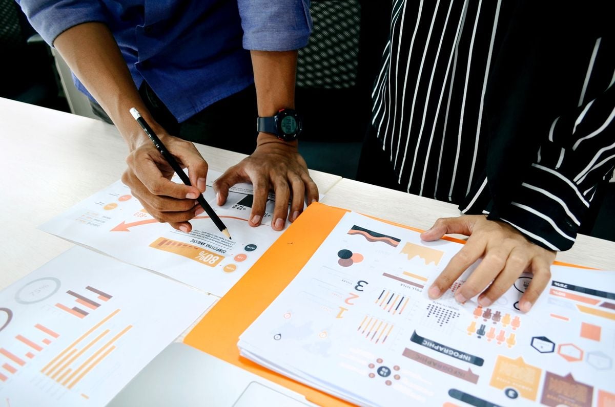 Two people reviewing printed marketing reports with charts, graphs, and infographics spread across a desk