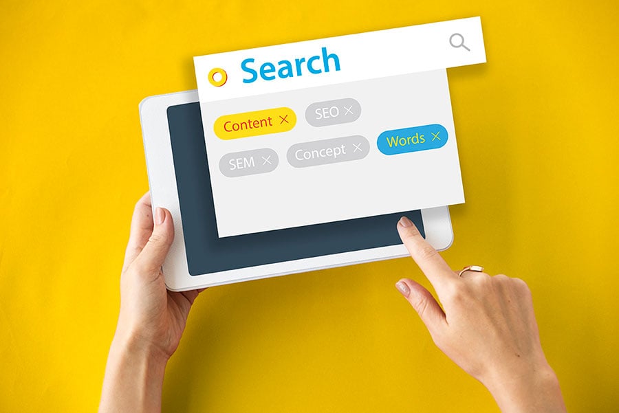 Hands holding tablet with search interface showing SEO, content, SEM, and keyword filters for digital marketing strategy research